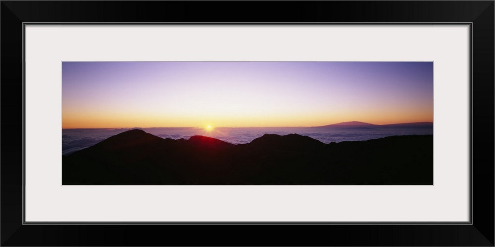 The sun begins to rise above the horizon and silhouettes a mountain range in the foreground of the picture.