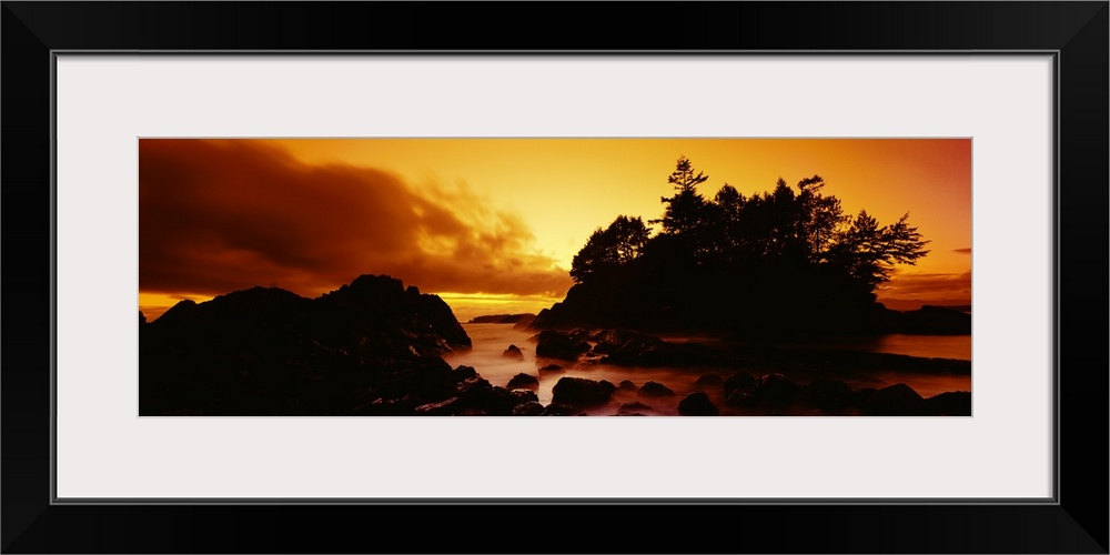 Panoramic photograph displays a sunburnt sky as the sun begins to set over the profile of a rocky shoreline in North America.