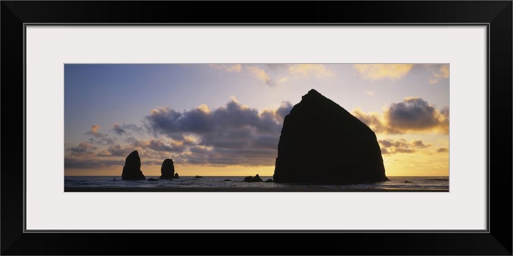 Large panoramic piece of the sunset that silhouettes rock formations in the ocean.