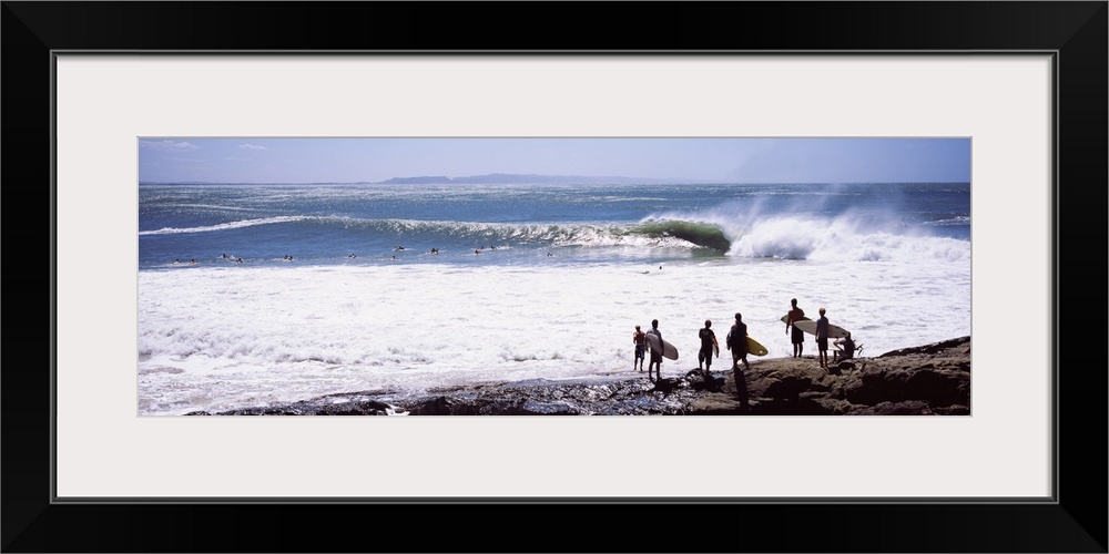 Panoramic photograph of beachgoers at water's edge with waves and ocean in the distance.