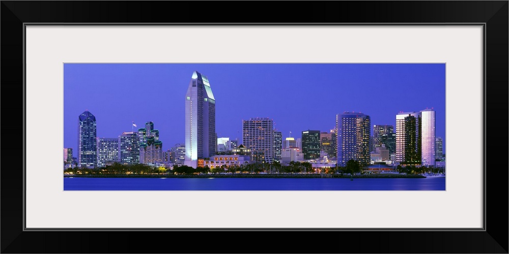 Skyscrapers in San Diego are illuminated and photographed in panoramic view from across a body of water.