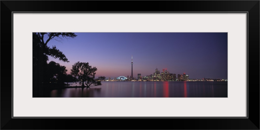 A panoramic photograph taken at twilight of the city skyline in the distance reflecting in the water around it, in the for...