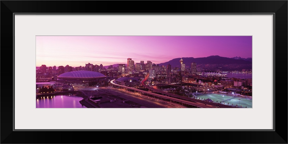 An aerial panoramic photograph taken of the skyline in Vancouver that has a purple hue from the sunset.