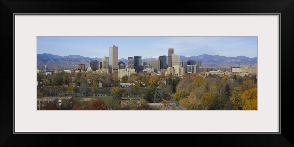 An urban city skyline nestled in a Rocky Mountain valley with a baseball field and several trees along the edge.