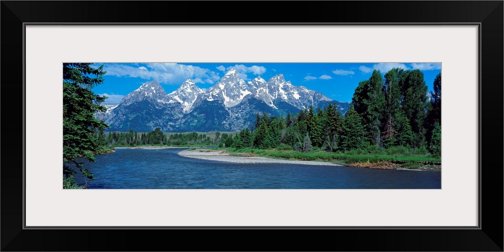 Panoramic photo of rugged mountains in the background of a wide river cutting through the landscape with trees on either s...