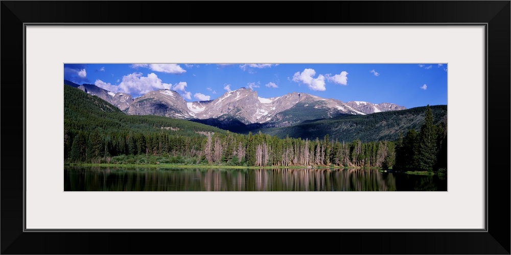 Long exposure of a body of water at the base of a mountain range, edged with a pine forest, under a partly cloudy sky in C...