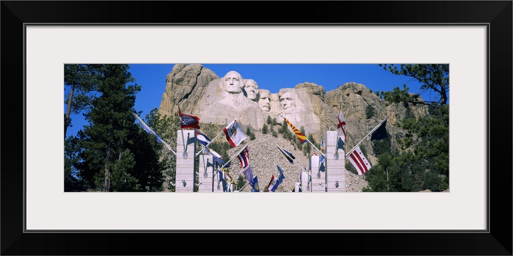 Panoramic photograph of iconic stone memorial carved in mountainside with column and flag lined walkway below.