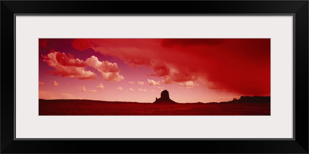 Giant horizontal photograph of a desert landscape beneath a vibrant sky with billowing clouds, a large rock formation on t...