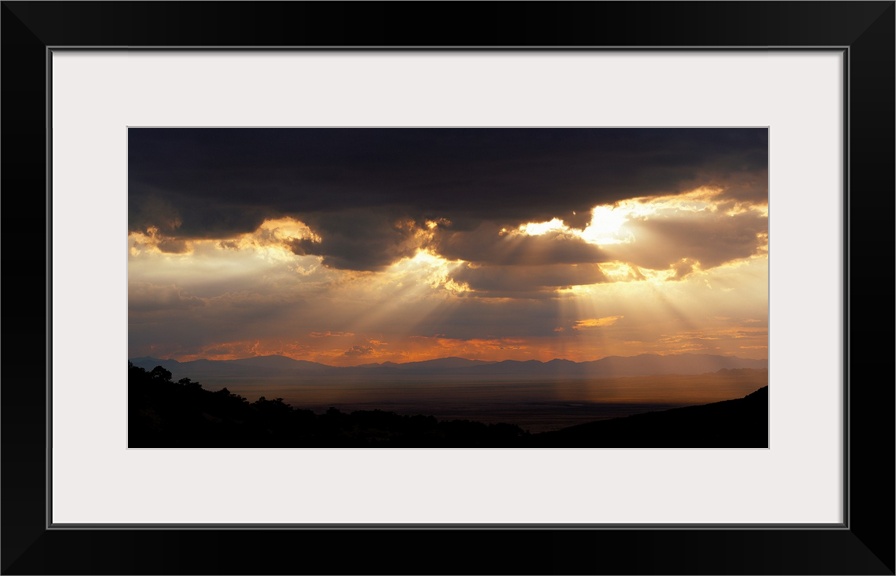 Horizontal, large photograph of sunlight beaming through a sky full of huge, dark clouds, over the Chiricahua National Mon...