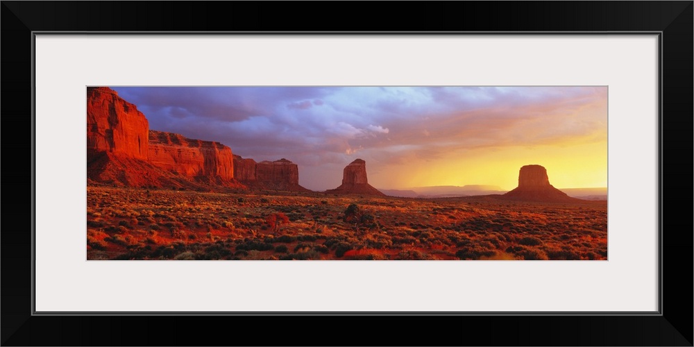 Large panoramic canvas of a desert scene with steep rugged terrain and rock structures at sunrise.