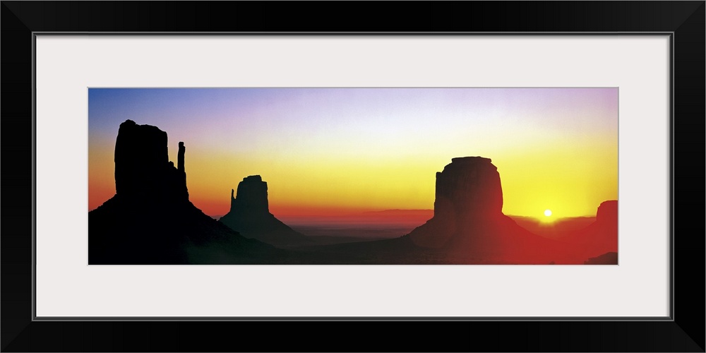 The sun begins to rise and silhouette Monument Valley in a wide angle view.