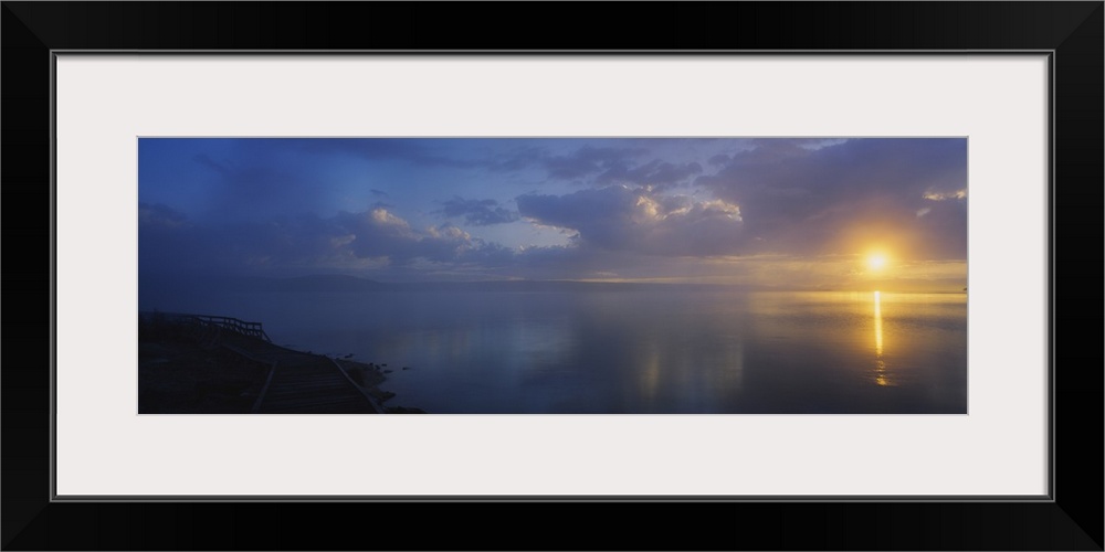 Panoramic photograph of walkway alongside ocean at dawn under a cloudy sky.