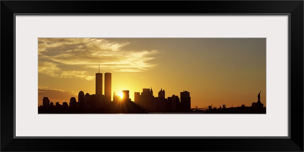 Panoramic photo of the sun rising right between two buildings in the silhouetted New York skyline, near the World Trade Ce...