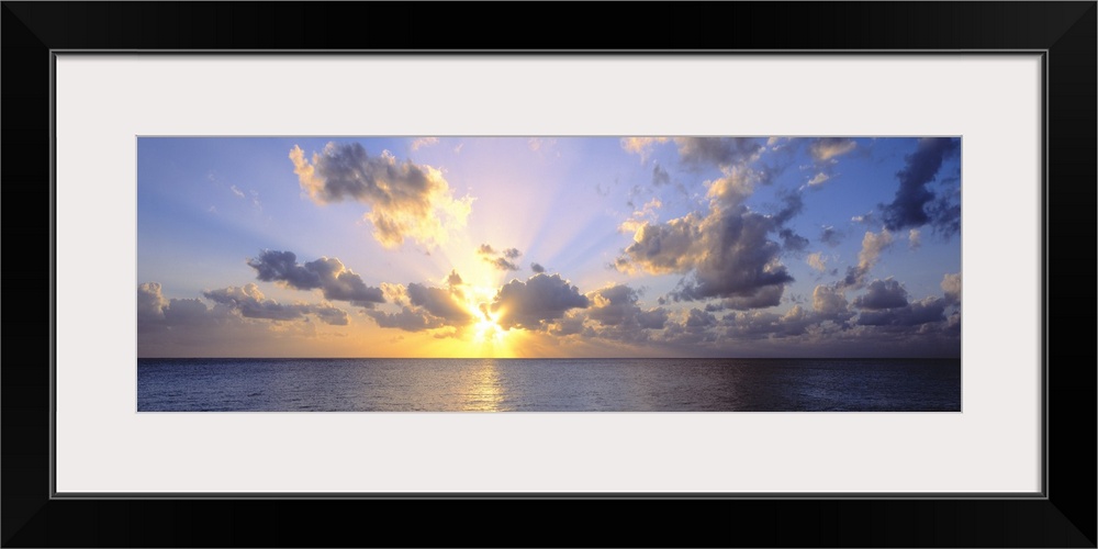 Giant panoramic photograph of the sun about to set in the distance from the perspective of a beachgoer looking out over th...
