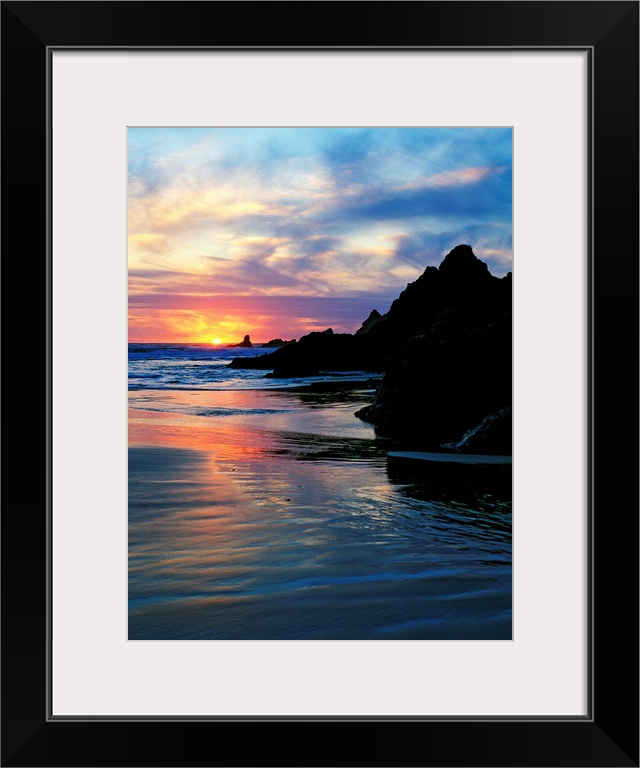 Sun below the horizon in a seascape with a rocky beach and waves.