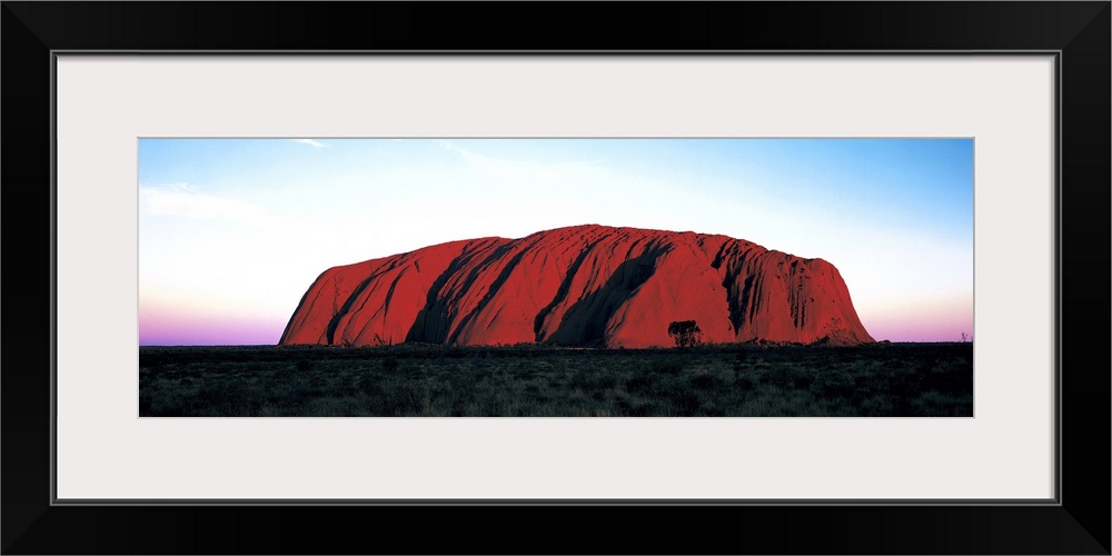 The Ayers Rock is photographed in wide angle view during a sunset which lines the horizon with warm colors.