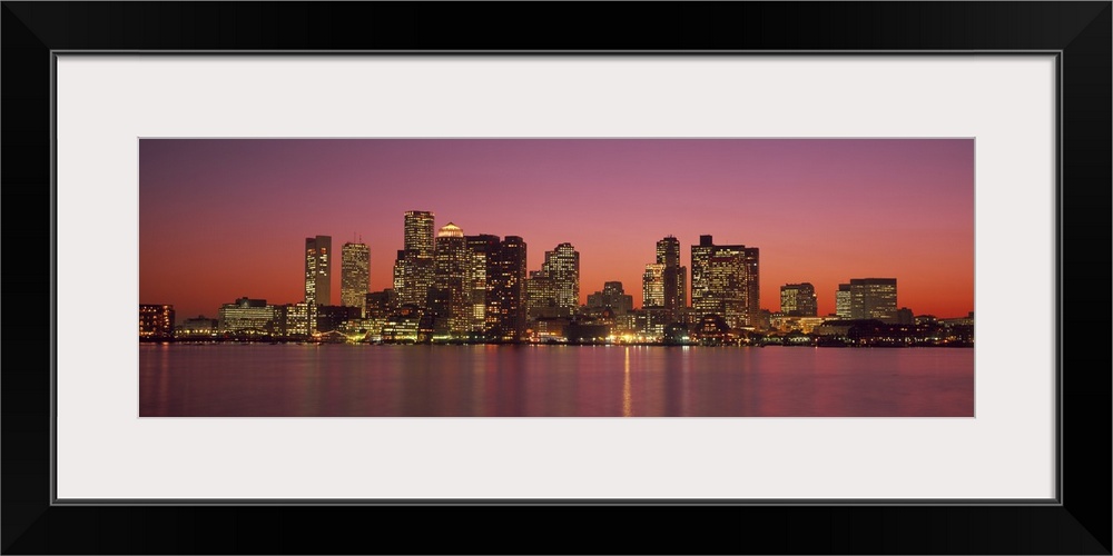 A Massachusetts city lights up at twilight over its blurred reflection in the waters of the bay.