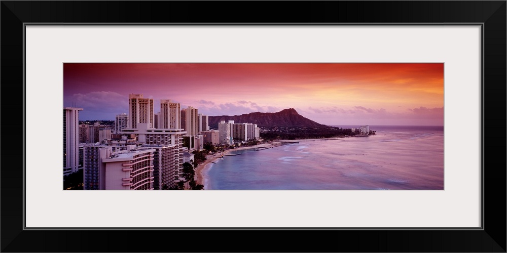 Rosy colors from the setting sun wash over the tropical island city next to the waterfront on Waikiki Beach, with Diamond ...