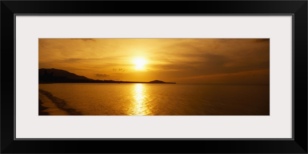 A beautiful sunset is photographed in panoramic view over the ocean water in Thailand.