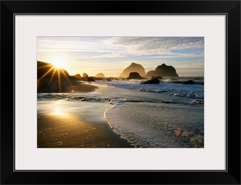 Panoramic photograph displaying a sunset over an ocean and sandy beach.  In the background you can see the waves hitting l...