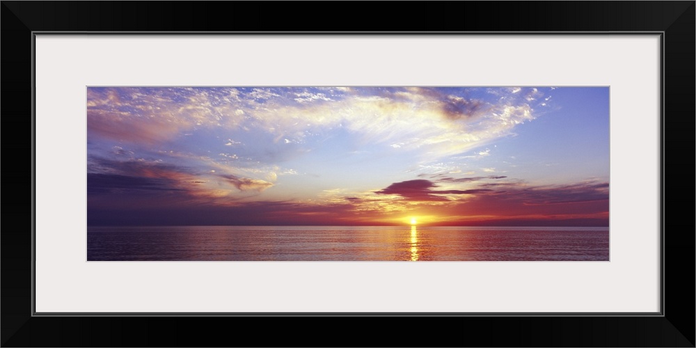 Large panoramic photograph of a sunset over the ocean with a cloud filled sky.