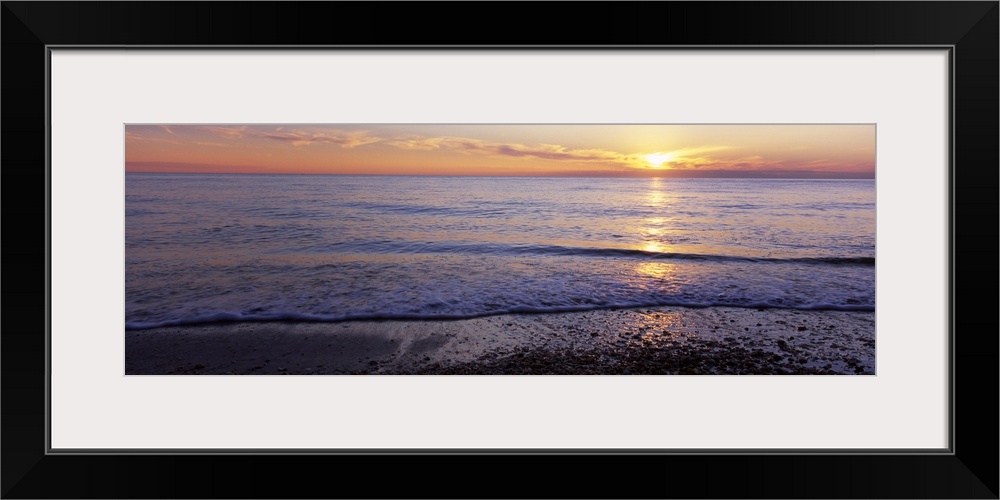 This is a panoramic landscape photograph of waves softly washing up on the shore of a sandy beach.