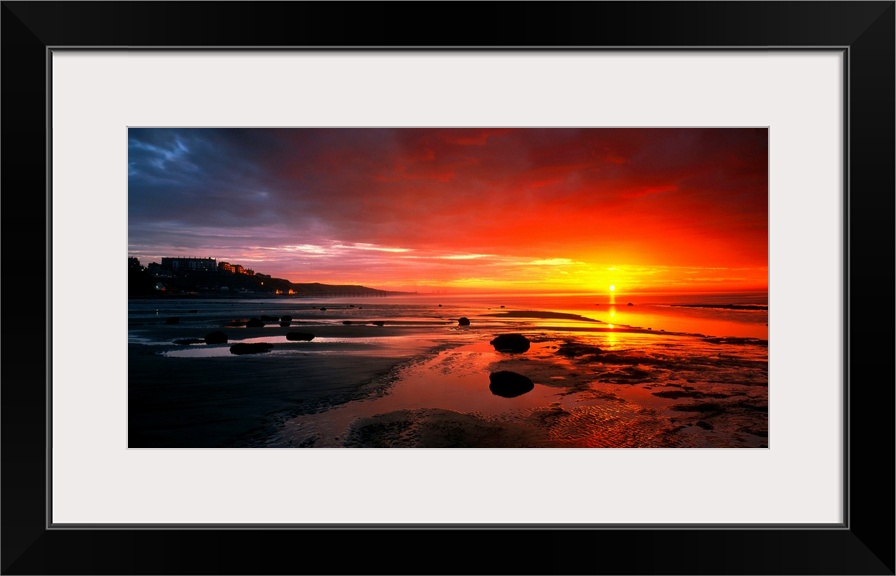 Panoramic photograph that captures a colorful sunset on the shores of England.  The calm beach is highly contrasted by the...