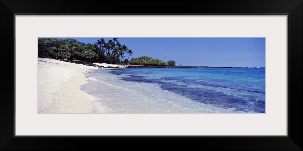 Clear ocean water rushes up onto an empty beach in Hawaii. Trees grow near the edge of the beach in the background of the ...