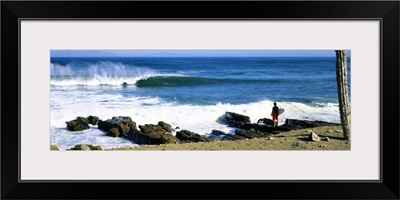 Surfer standing on the beach and looking at surf, Isla Natividad, Baja California, Mexico