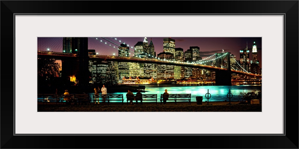 Manhattan lights reflecting in the East River under the Brooklyn bridge while people sit on benches watching the view.