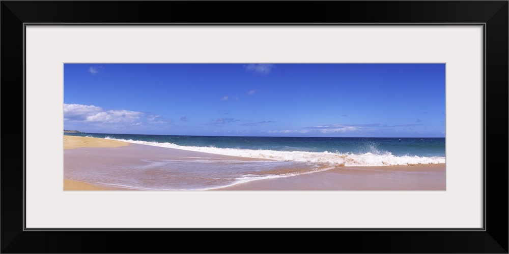 This is a landscape panoramic photograph of a flat sandy shoreline and a calm sea with few clouds in the sky.