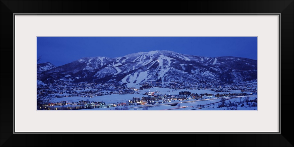 Wide angle shot of an illuminated ski lodge with mountains pictured just behind it.