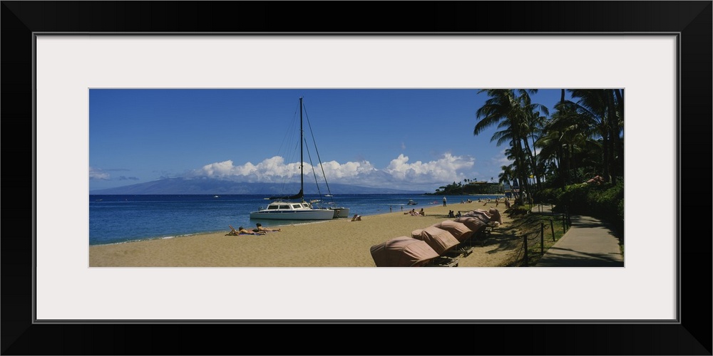 Panoramic photograph of shoreline filled with beachgoers and docked sailboats under a cloudy sky.