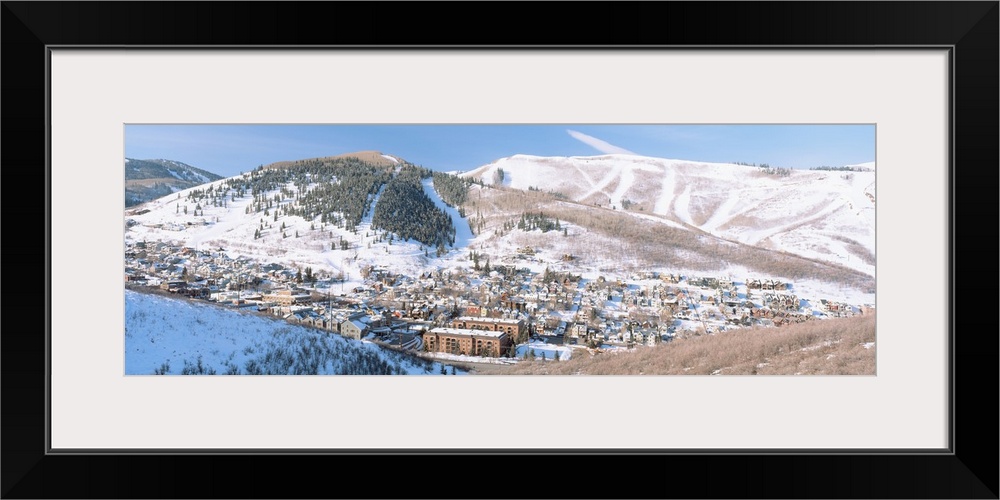 Wide angle photograph on a large canvas of a distant town in a valley, surrounded by a snow covered mountain landscape in ...