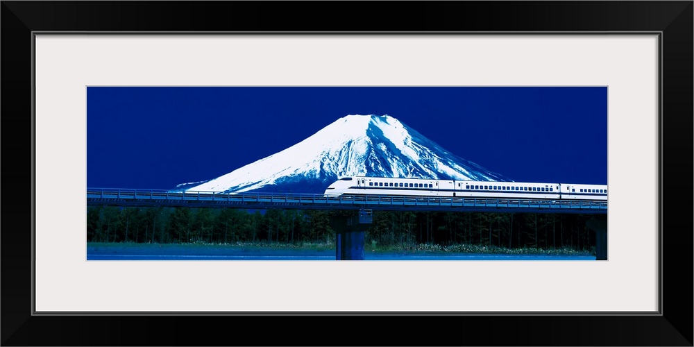 Panoramic photo on canvas of a train going across a bridge above water with a snowy mountain the background.