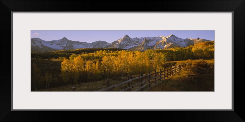 Wide angle photograph on a large canvas of a wooden fence running through a golden fall landscape of Dallas Divide, the sn...