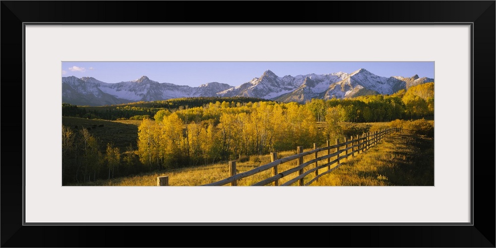 Panoramic view of the distant Rocky Mountains in the Midwestern United States, with a forest and a rustic fence in autumn.