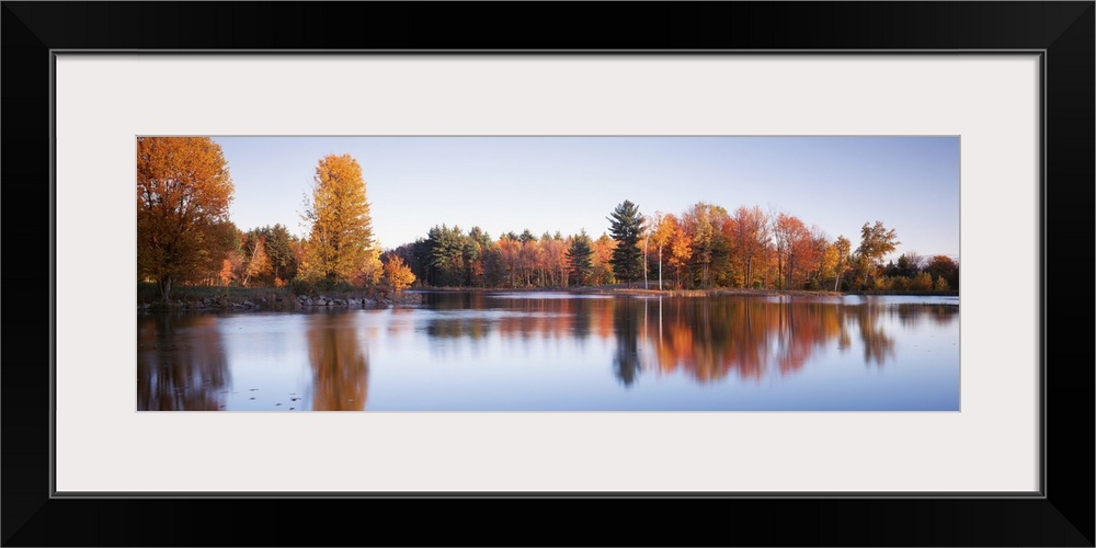 This photograph is taken behind a body of water of fall colored trees that line the other side of the lake.