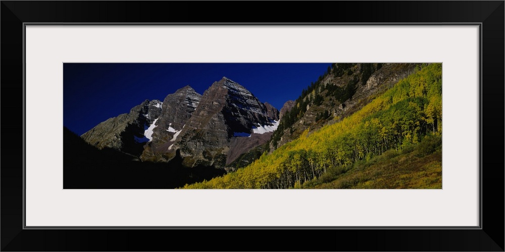 Panoramic wall art of a photograph looks up a mountainside covered with trees and mountain peaks beyond.