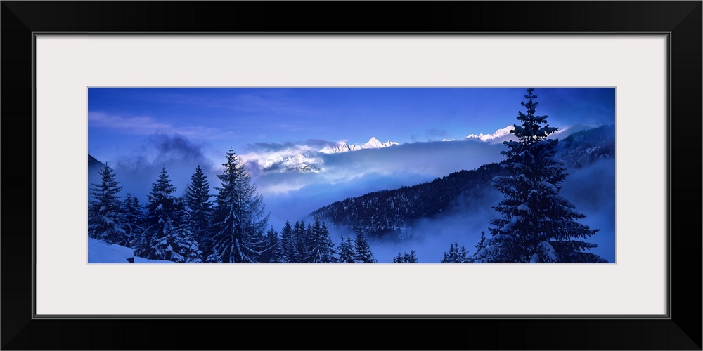 Wide angle photograph of a frozen landscape of snow covered trees and frosty hillsides, beneath a deep blue sky in Simplon...