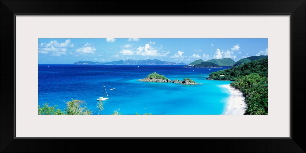 Panoramic photograph of a couple boats sitting in the clear waters of Trunk Bay in the Virgin Islands.  The mountains in t...
