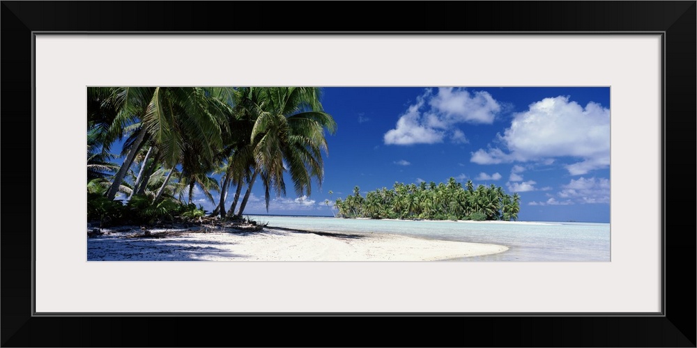 Palm trees leaning over the white sands and shallow water of the tropical South Pacific island on a perfect sunny day.