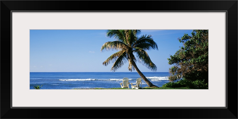 This is a panoramic photograph of a grassy lawn that grows up the shoreline where two lounge chairs face the sea in the sh...