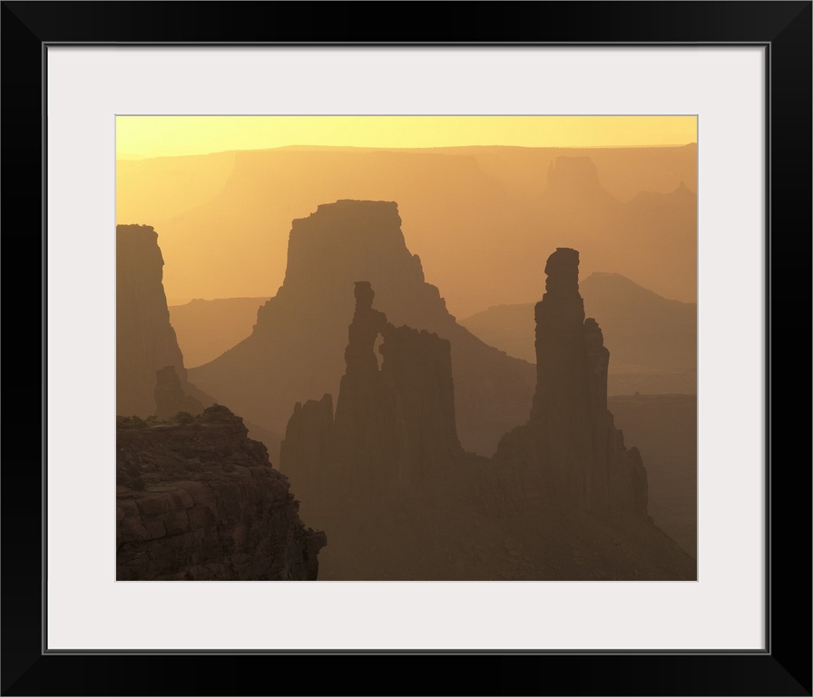 The large rock formations in Canyonlands National Park is silhouetted by the sunset that is out of view.