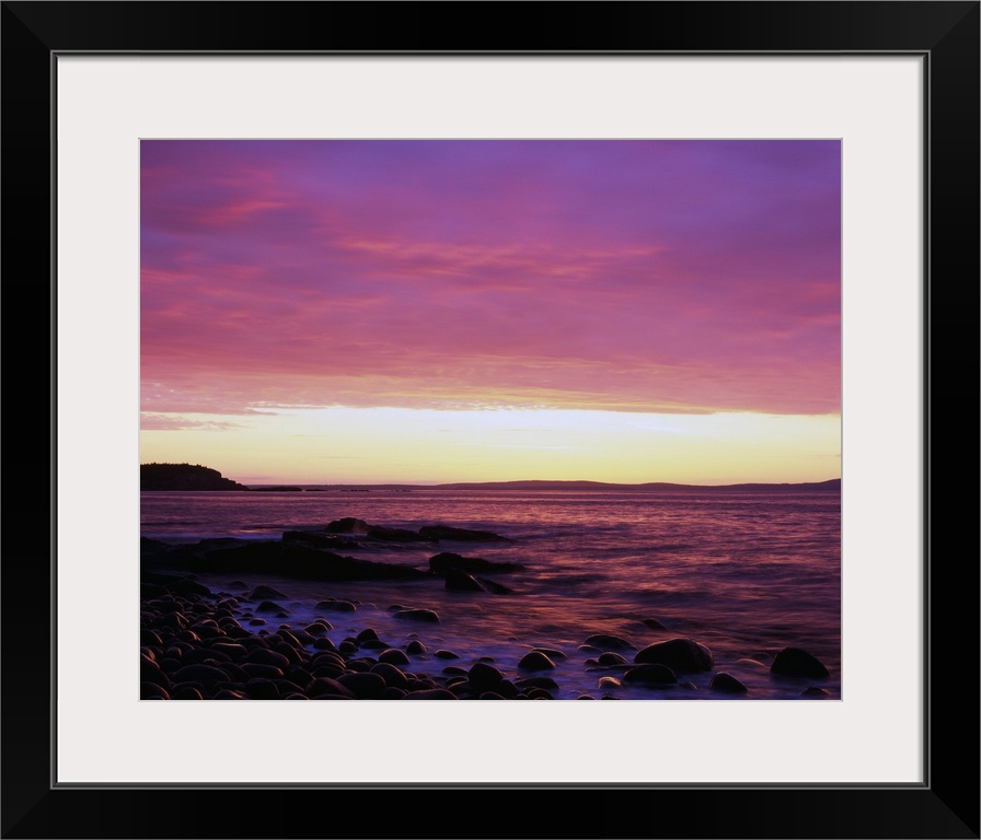 This large piece is a picture taken of the sun rise off the coast of Maine. Rocks line the edge of the water and reach out...