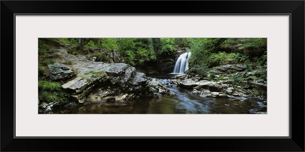 A waterfall in the distance is photographed as it flows into a pool of water that rushes toward the foreground of the pict...