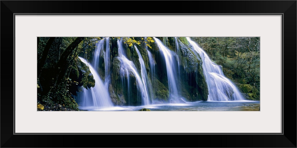 Wide angle, large wall picture of a giant waterfall surrounded by a forest in Jura, France.