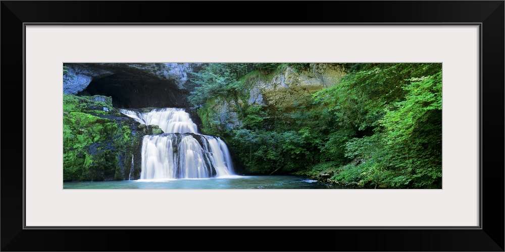 A large waterfall falls out of a cave into the Lison River in Jura, France.