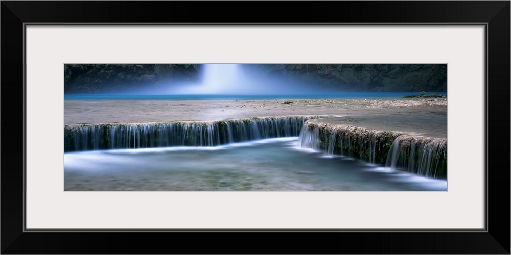 This is a panoramic, time lapsed photograph of water flowing over shallow waterfalls in a desert oasis.