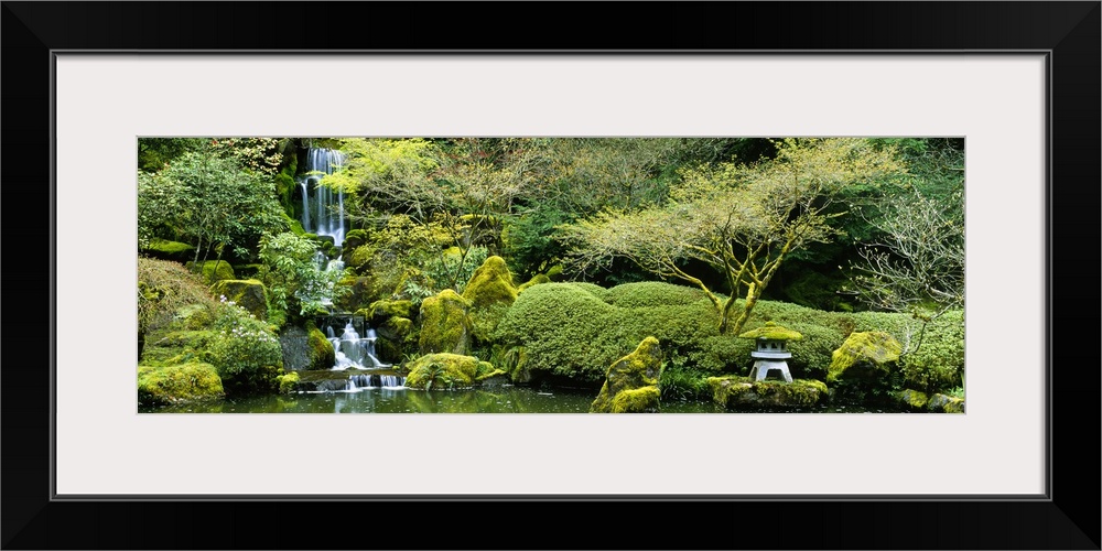 Wide angle photograph taken of a small waterfall inside a Japanese garden. It's surrounded by lush green foliage.